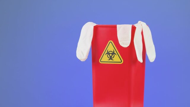 Cautious medical clinical waste management container with red biohazard disposal warning holds protective white glove under strict safety precaution