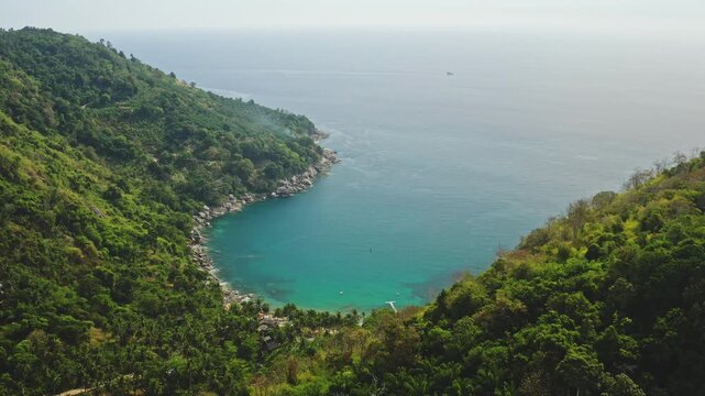 Tropical island beautiful turquoise bay surrounded by lush green tropical hills merging with the Andaman Sea on the Phuket coastline, highlighting serene nature beauty. Aerial view drone flight