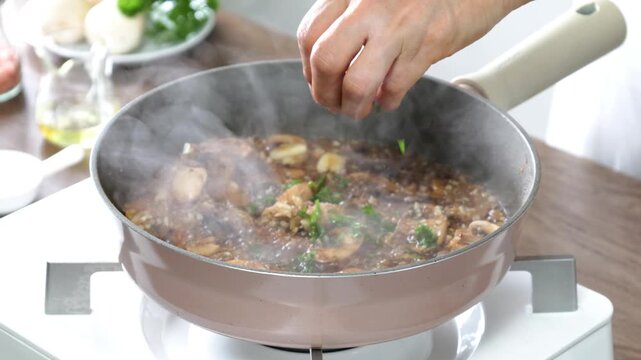 Fresh parsley is sprinkled over a simmering mushroom garlic sauce in a skillet, creating a rich homemade dish with aromatic herbs and visible steam. Close-up cooking scene in a modern kitchen, perfect