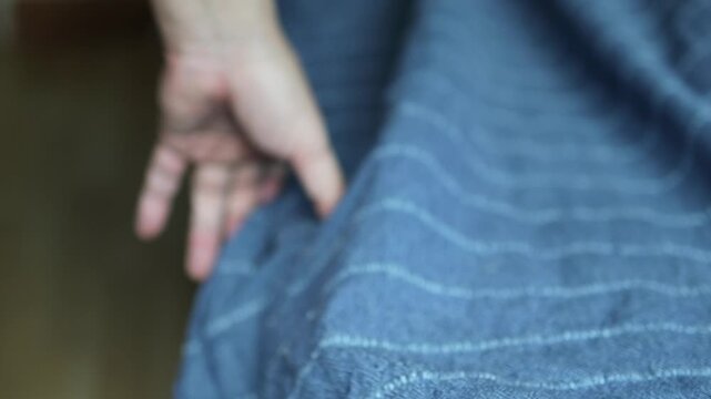 Horizontal 4K close up video of a man hand pulling a blue bedsheet over the mattress and stroking it smoothly to tidy up the bed