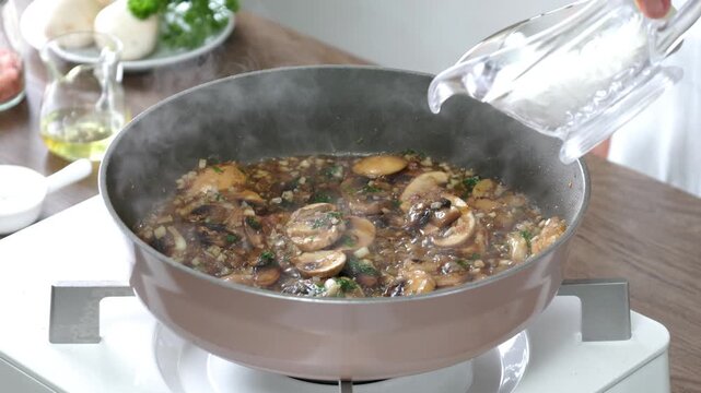 Pouring fresh cream into a skillet of saut&eacute;ed mushrooms and aromatic herbs, creating a rich and creamy mushroom sauce. Close-up cooking process with steam rising in a bright home kitchen.