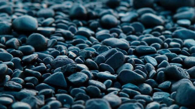 Close up of dark stones cover the ground. Cool tones dominate the scene.