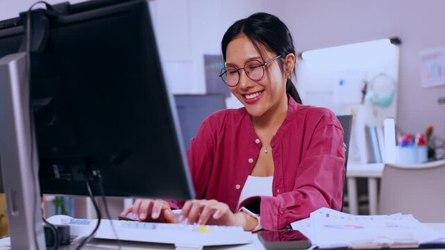 Woman Using Computer In Office With Keyboard Glasses Desk Work Smiling Professional Technology Typing On Modern Workplace Monitor Paperwork Phone Whiteboard Casual Shirt