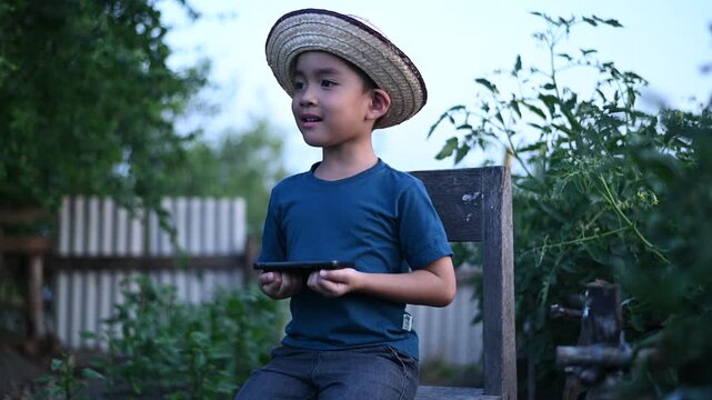 4 Year Old ASEAN Boy Using Tablet in Vegetable Garden Exploring Smart Farming AI Technology and Future Food Security Concept
