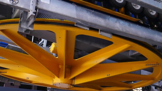 Low-angle close-up of a massive yellow six-spoke metal sheave wheel for a cable car station, mounted beneath a steel beam with guide rollers for the rope system 4k video