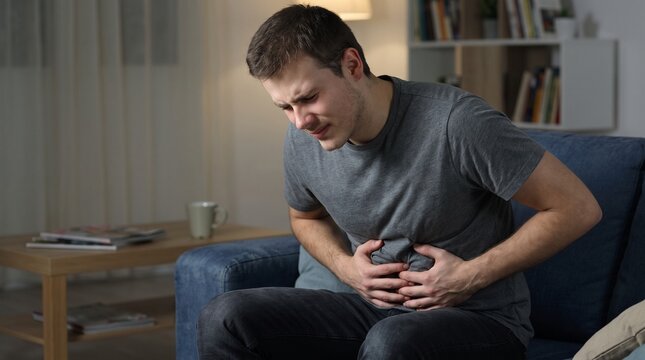 Young man holding his stomach in severe pain on sofa at night