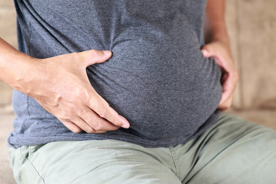 Overweight man holding belly fat, representing obesity, excess body fat, weight loss, unhealthy lifestyle, diet, fitness, body transformation, and health awareness