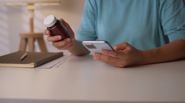 Asian mature woman reading the label on a medicine container and using a smartphone.