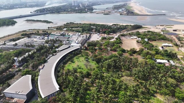 Wide aerial panorama of a fishery and seafood processing facility near Kovalam Estuary, featuring industrial infrastructure, estuary backwaters, coastal vegetation, and the Bay of Bengal shoreline.