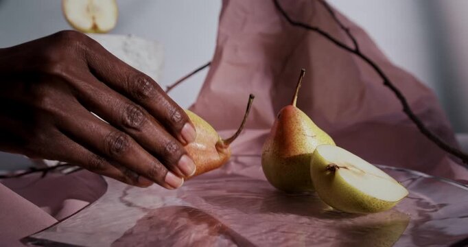 Hand arranging fresh pears and sliced pear on table with decorative styling. Ripe fruit composition showcasing natural texture and rustic presentation in daylight