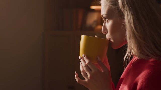Caucasian young adult woman holding yellow mug with steaming drink, smelling and sipping beverage. Clip is ideal for commercials promoting mental wellbeing, self-care, or autumn lifestyle brands