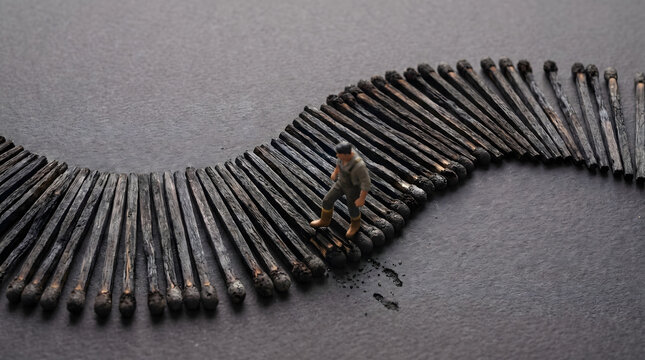 Miniature figure walking on a path of burnt matches symbolizing persistence and life journey