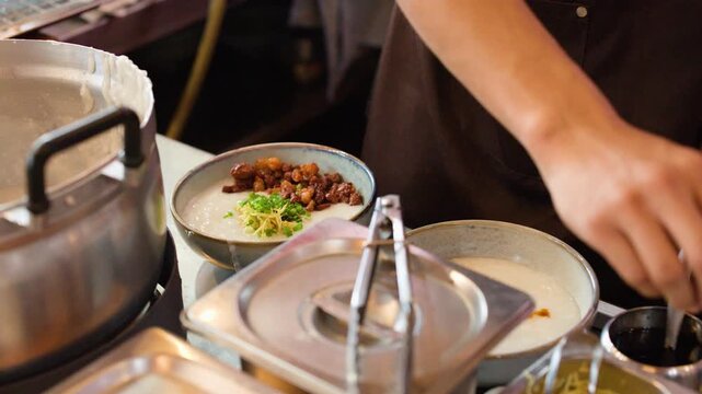 Asian Chef Garnishing Rice Porridge with Scallions and Ginger