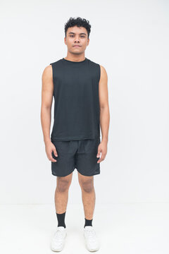 A young Southeast Asian man stands upright with a confident expression, wearing a black athletic outfit and sneakers in a minimalist studio.