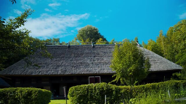 青空と緑に囲まれた大きな茅葺き屋根の古民家全景 4Kシネマティック映像素材
