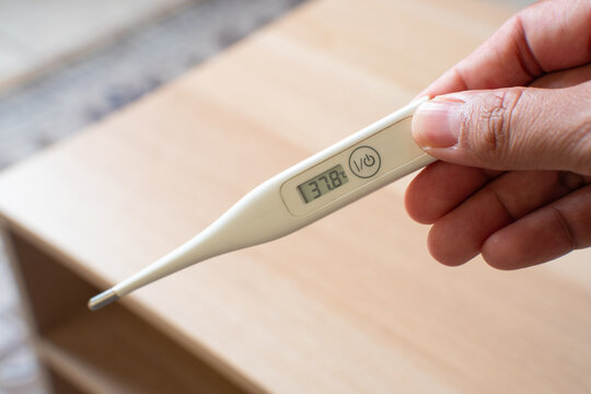 Close-up of a hand holding a digital thermometer displaying a high temperature, representing fever, illness, body temperature measurement, and healthcare monitoring.