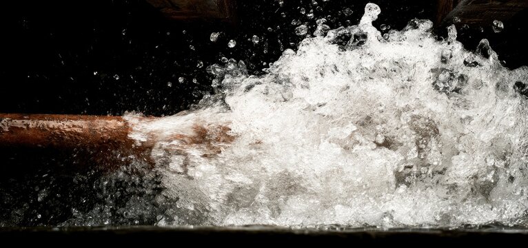 Powerful water jet spraying from a pipe with a dark background.
