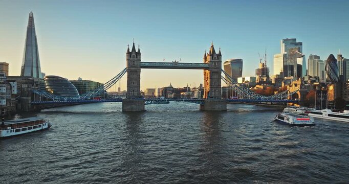 Tower Bridge framed by iconic skyscrapers The Shard and The Gherkin. City Cruises boats navigating River Thames during a golden hour sunset. Aerial drone shot of main tourist attraction, visit England