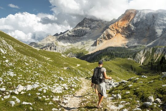 Male hiker with backpack walking dirt trail green alpine meadow majestic mountain peaks background Malga Rossalm Dolomites Italy summer adventure travel lifestyle