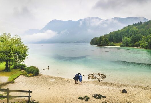 Male and female is standing by the Bohinj lake and looking tothe lake while its raining.Slovenia