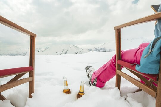 Couple relax sit on chairs in snowy ski resort with beer bottle, concept of leisure, winter holiday, relaxation, carefree lifestyle, freedom, cozy outdoor relaxation moment