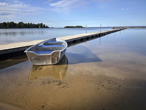 Lonely boat on a sandy beach next to a jetty. Blue sky and calm water surface, V&auml;nern, Mellerud, Dalsland, Sweden