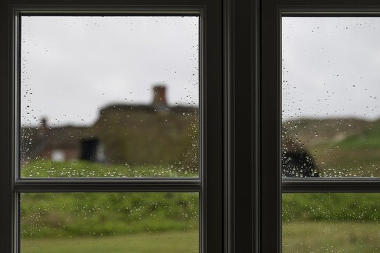 View through window panes with raindrops beading, blurred traditional thatched Danish houses in the background, Houvig, North Sea, Denmark