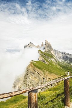 Wooden safety railing fence overlooking dramatic mist covered Seceda mountain peaks steep cliff edge danger zone alpine nature park Dolomites Italy. Minimizing human footprint by protecting vulnerable wildlife