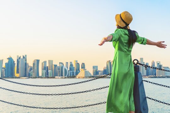 Woman traveler visitor standing with open arms at waterfront facing Doha skyline across bay symbolizing freedom urban lifestyle travel Middle East modern city concept