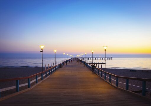 Illuminated romantic vintage Palanga pier after sunset with people walking in beautiful summer evening. Lithuania summer holiday landmarks destination. Palanga.Lithuania