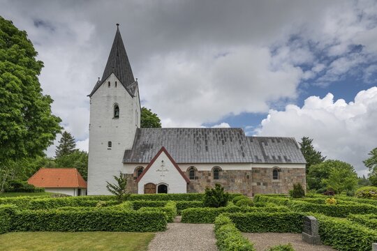 Well-maintained cemetery with low hedges, side view of an old Romanesque stone church, Husby Kirke, Holstebro Municipality, Denmark