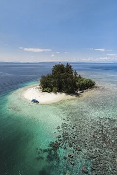 Aerial view of a small tropical island with turquoise water, white sandy beach, a boat and a proposed reef, Raja Ampat, West Papua, Indonesia