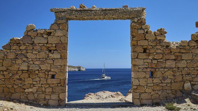A stone arch with a view of a sailboat on the sea under clear blue sky, Palio Ergostasio Kaolini, Old Kaolin Loading Station, Ruins, Firopotamos, Fishing Village, North Coast, Beach, North Coast, Milos, Cyclades, Greek Islands, Greece