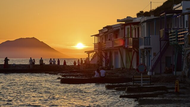 Evening atmosphere by the sea with silhouettes and colorful buildings at sunset with warm light, boathouses, boat garages, Syrmata, fishing village, coastal town, climate, Milos, Cyclades, Greek islands, Greece
