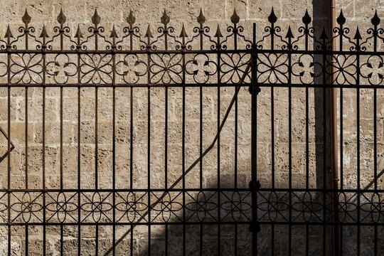 Cast iron fence with ornamental spikes, casting shadows on a stone wall, Palermo, Sicily, Italy