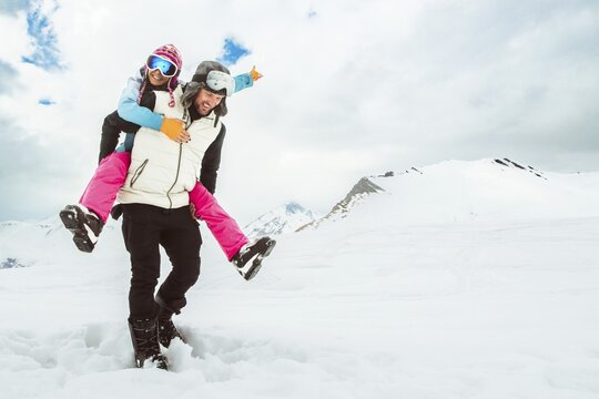 Background of laughing couple enjoy romantic piggyback ride in snowy winter landscape, expressing happiness, love, freedom, carefree vacation, joyful relationship, bonding, playful adventure
