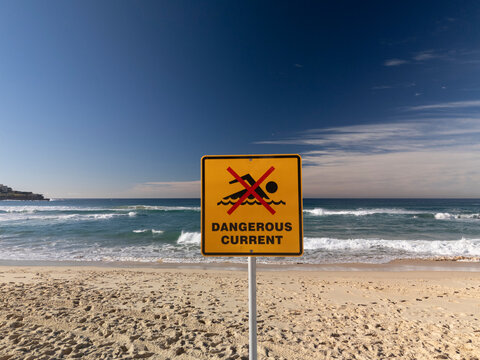 No swimming dangerous current sign at beach on perfect sunny day with blue sky and waves.