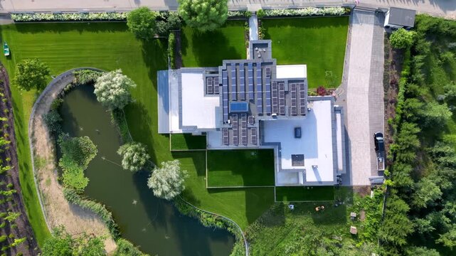 A luxury modern villa with solar panels, pond, and lush lawn in a suburban estate, aerial top down view from drone. 