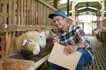 Asian Farmer Checking Sheep with clipboard in Barn © Yazid Nasuha