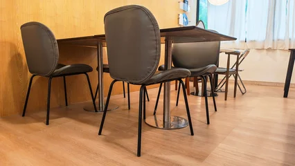 A minimalist dining area features a sleek table surrounded by stylish Grey leather chairs and wooden tables interior set in minimalist cafe showcasing contemporary design in a warm, inviting space. © Chatchaa