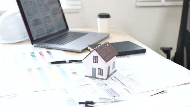Architect reviewing construction plans at a modern office desk with blueprints, laptop, and engineering tools for a building project.