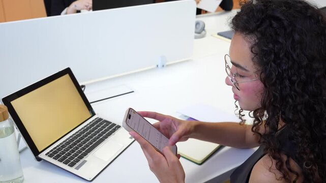 Businesswoman with curly hair sending a text message on her smartphone in an open office