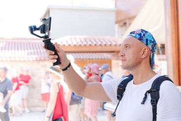 Fototapeta premium Bald Man Films with Smartphone Gimbal at Crowded Tourist Street Kaleici