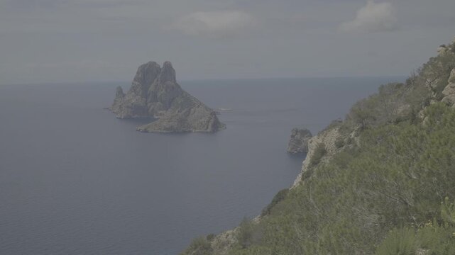 A wide shot of Es Vedr&agrave; island off Ibizas coast showcasing clear blue waters and rugged cliffs under a calm sky atmospheric lighting vibrant colors smooth motion LOG