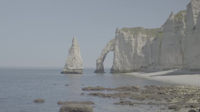 Breathtaking wide shot of Etretat chalk cliffs against a calm blue sea under clear skies showcasing natural beauty cinematic quality dynamic movement atmospheric lighting LOG