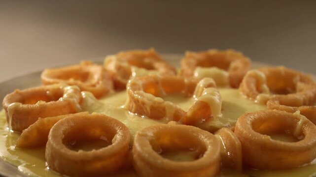 A plate of crispy golden onion rings covered in a rich and creamy cheese sauce