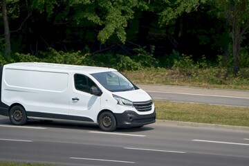 White minibus on a country road surrounded by grass fields © AlexGo