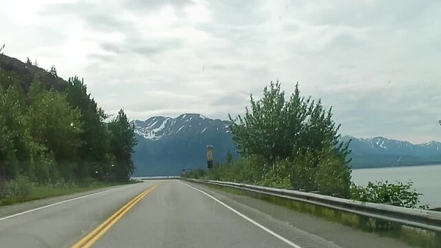 1080p, 30fps. Windshield timelapse driving along Turnagain Arm on the Seward Highway near Anchorage, Alaska, with coastal mountains and tidal flats passing by.