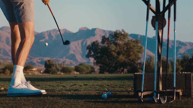 A tight close up of golfer hitting ball on driving range in slow motion with desert mountain backdrop