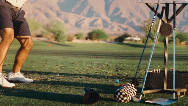 A low close up of golfer hitting drive on driving range in slow motion,, desert mountains behind in golden light